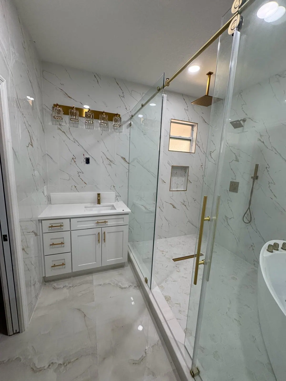 Luxury bathroom with marble-look tile, gold fixtures, and a glass shower